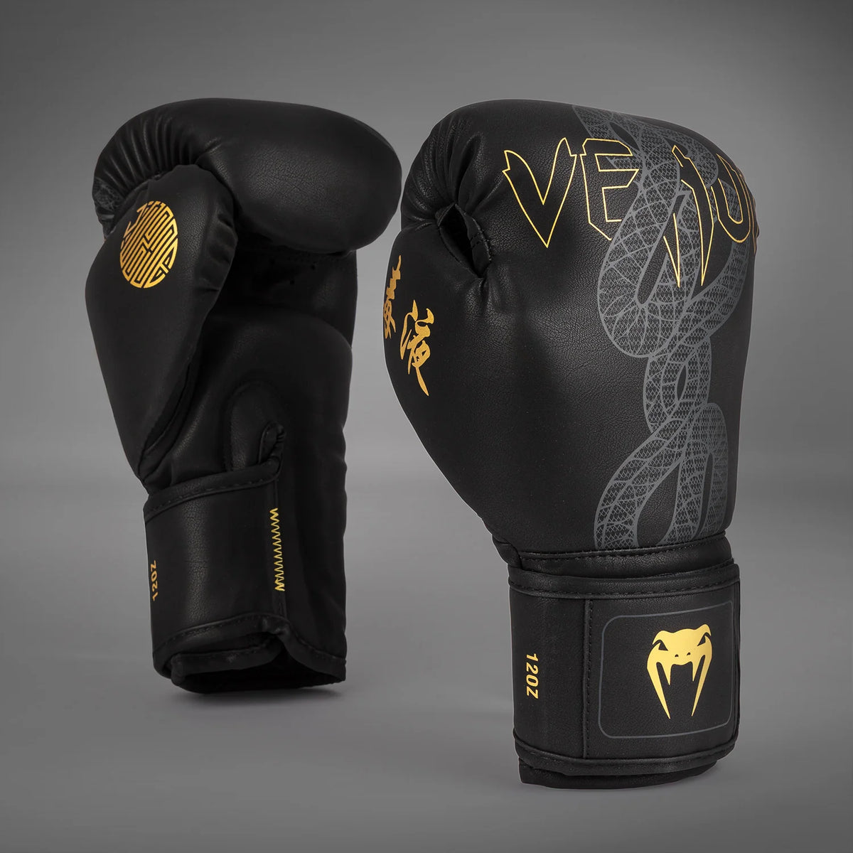 Angled pair of Venum Serpenti Boxing Gloves in Black/Silver/Gold showing the silver serpent graphic, gold branding and palm-side profile