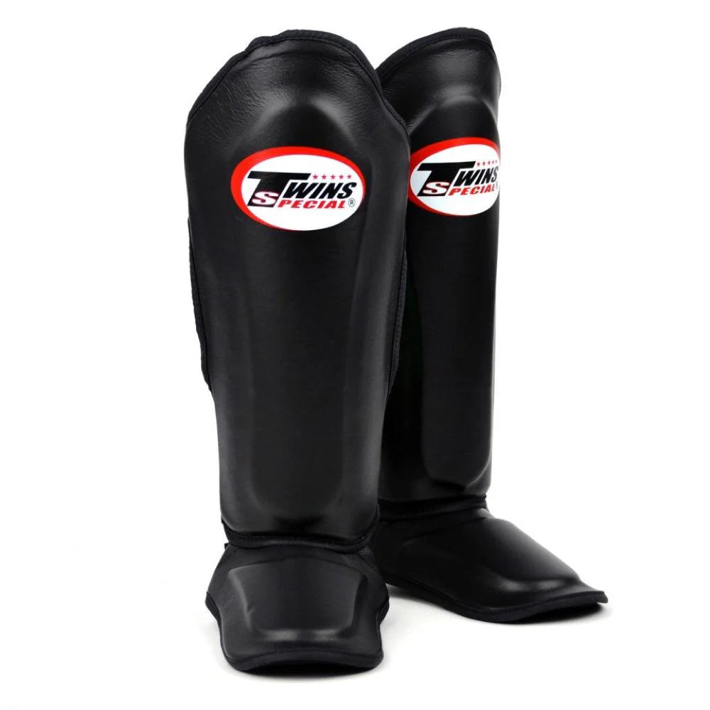 Side profile of Twins SGL10 Black shin guards showing ergonomic contoured fit and metal-free Velcro straps.