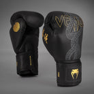 Angled pair of Venum Serpenti Boxing Gloves in Black/Silver/Gold showing the silver serpent graphic, gold branding and palm-side profile