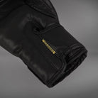 Close-up of the Venum Serpenti boxing glove cuff and palm area showing black PU construction and contrasting gold stitching