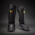 Angled pair of Black/Gold Venum Streamline Shin Guards showing the contoured shin and foot profiles