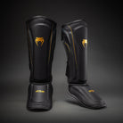 Angled pair of Black/Gold Venum Streamline Shin Guards showing the contoured shin and foot profiles