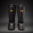 Venum Streamline Black/Gold shin guards showing the padded shin panels and connected instep protectors