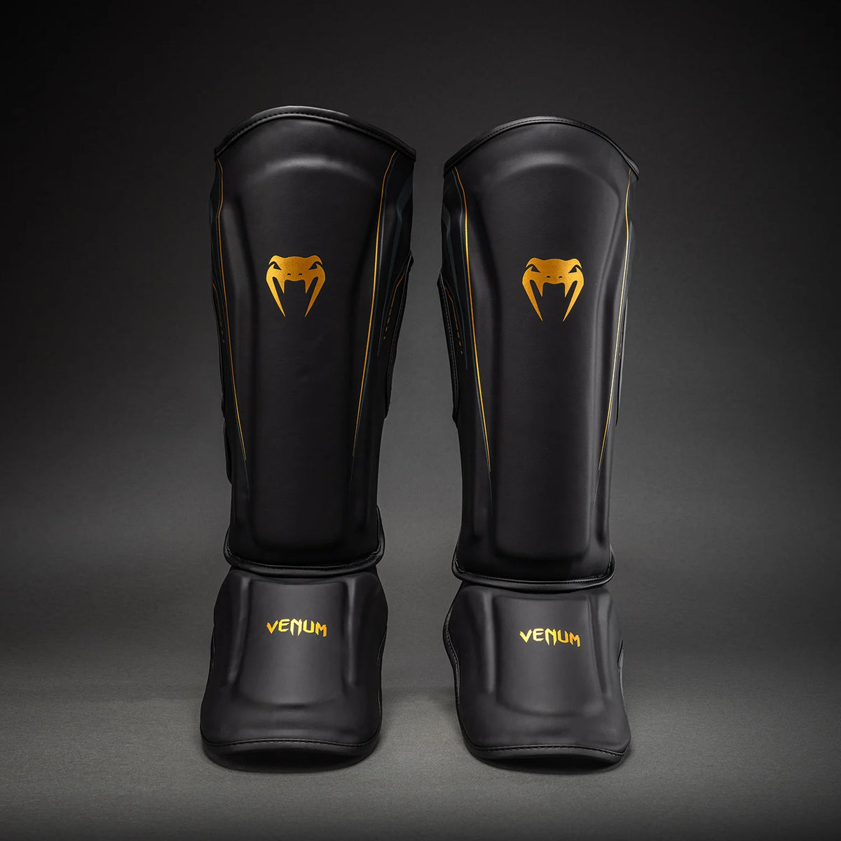 Venum Streamline Black/Gold shin guards showing the padded shin panels and connected instep protectors